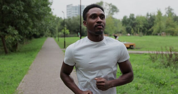 Coureur d'homme afro-américain actif s'entraînant seul, courant dans un parc de la ville vide. Entraînement du matin. Concept de mode de vie sain.