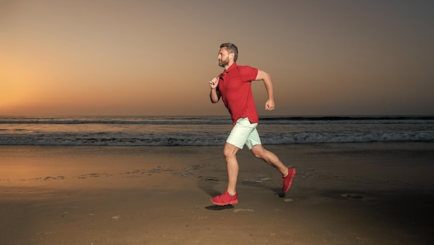 Coureur d'homme athlétique courant sur l'endurance de la plage d'été au coucher du soleil