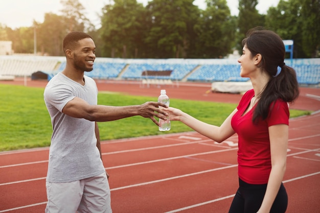 Coureur d'homme donnant une bouteille d'eau à sa petite amie après s'être entraîné sur la piste du stade