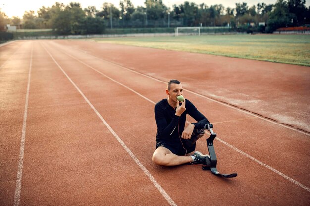Un coureur avec une jambe prothétique se détendant avec de la musique et mangeant une pomme au stade