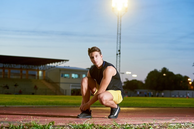 Coureur de jeune homme attachant des lacets sur le stade.