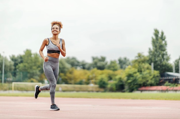 Un coureur mince aux cheveux bouclés court dans le stade par temps nuageux et se prépare pour un marathon