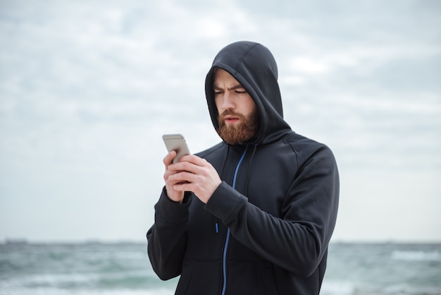 Coureur avec téléphone sur la plage en regardant le téléphone