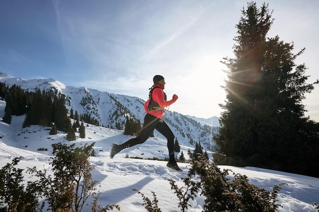 Photo coureur de trail femme qui court dans les montagnes d'hiver sentier sur la neige femme en cours d'exécution dynamique athlète vue latérale