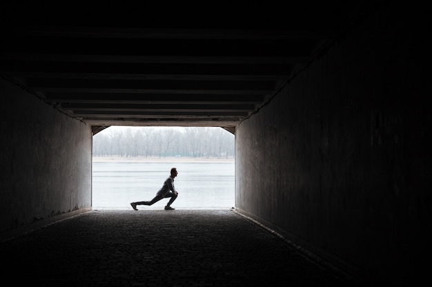 Coureur en vêtements de sport gris s'échauffant dans un tunnel. Image pleine longueur