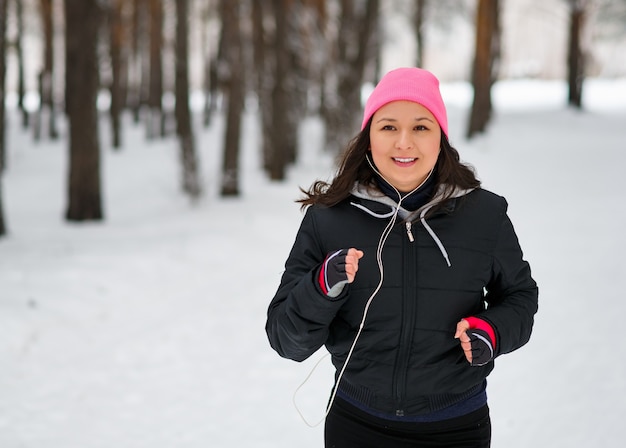 Coureuse de jogging dans la forêt d'hiver froid portant des vêtements de course sportifs chauds et des gants d'écouteurs.