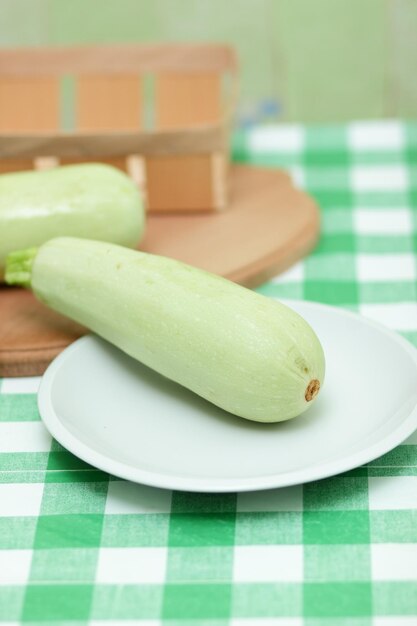 Une courgette entière sur une plaque blanche et une planche de bois sur une nappe verte Gros plan de légumes sains