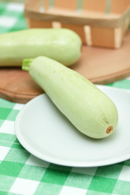 Une courgette entière sur une plaque blanche et une planche de bois sur une nappe verte Gros plan de légumes sains