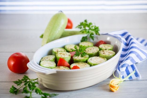 Courgettes crues aux tomates préparées pour la cuisson sous forme de céramique sur une table en bois