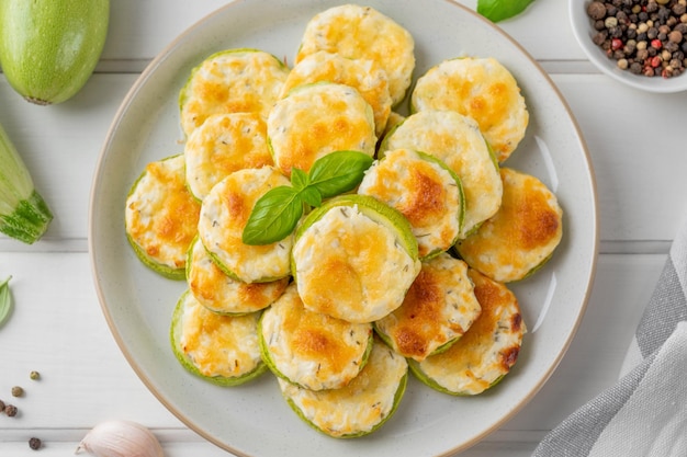 Courgettes cuites au four avec de l'ail au fromage et des herbes fraîches sur un fond en bois blanc Mise au point sélective