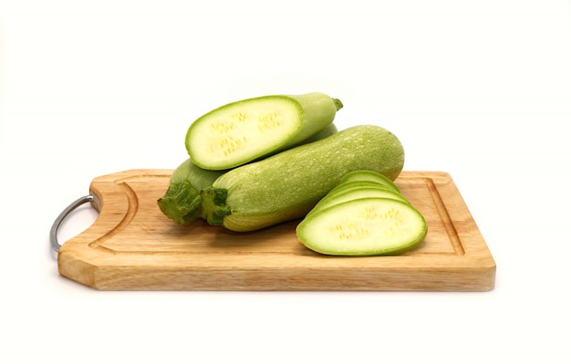 Courgettes entières et coupées sur une planche à découper sur un fond clair. Fermer.