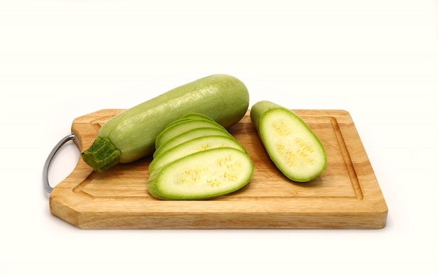 Courgettes entières et coupées sur une planche à découper sur un fond clair. Fermer.