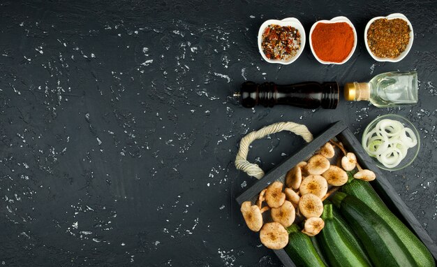 Courgettes fraîches, champignons, épices et herbes sur un tableau noir en vue de dessus avec espace de copie