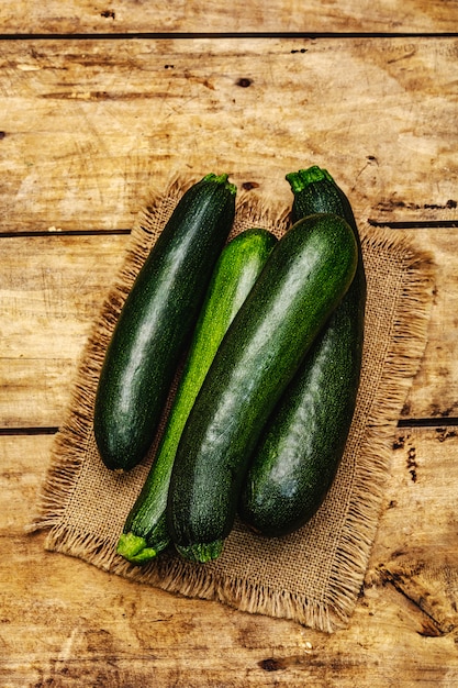 Courgettes vertes entières non pelées. Nouvelle récolte, sur un sac, fond de planches de bois, vue du dessus