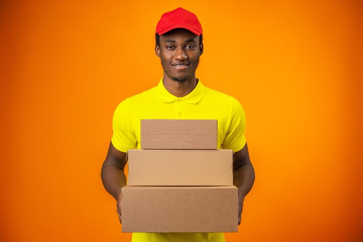 Photo courier noir souriant portant un uniforme dans une boîte de détention dans un studio orange