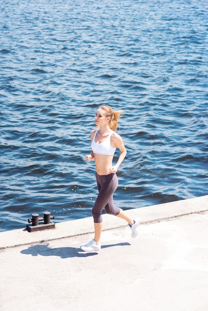 Courir, c'est sa vie. Jeune femme en vêtements de sport le long de la berge