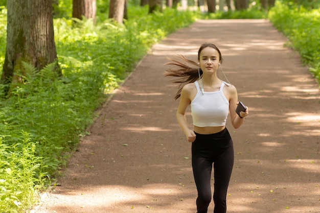 Courir faire du sport garder la forme Fille court dans les écouteurs dans le parc parmi les arbres