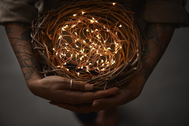 Couronne de brindilles et lumières de Noël dans les mains des femmes sur un fond sombre à plat