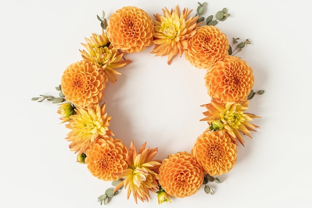 Couronne de cadre espace vide rond faite de beaux boutons de fleurs de dahlia orange et de branches d'eucalyptus sur blanc. Mise à plat, vue de dessus