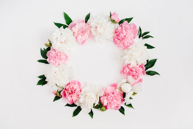 Couronne de cadre de fleurs de pivoine rose, de branches, de feuilles et de pétales avec un espace pour le texte sur fond blanc. Mise à plat, vue de dessus