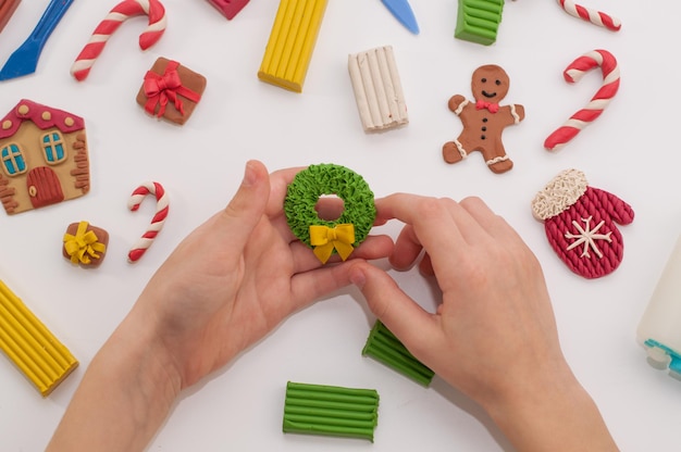 Une couronne dans les mains d'un enfant et d'autres métiers de la pâte à modeler pour Noël sur fond blanc