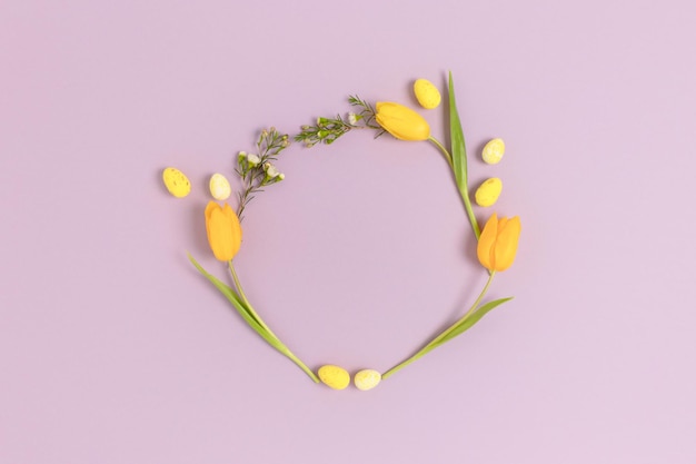 Couronne faite d'oeufs de pâques et de fleurs sur fond pastel violet