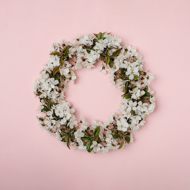 Photo couronne de feuilles de cerisier en fleurs et de feuilles vertes sur fond rose. concept créatif minimal de joyeuses fêtes de printemps.