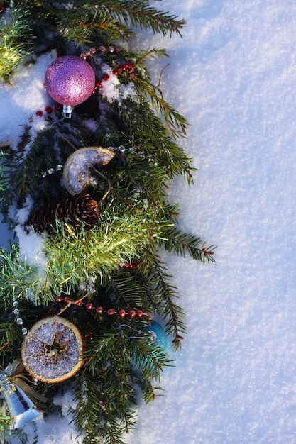 Couronne de Noël décorée de tranches d'orange sèches et de boules colorées sur fond de neige blanche.