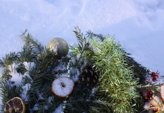 Couronne de Noël décorée de tranches d'orange sèches et de boules colorées sur fond de neige blanche.