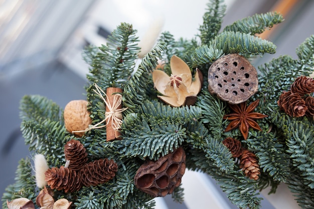 Couronne de Noël faite de branches de sapin naturel accroché au dossier de la chaise blanche. Couronne avec des ornements naturels: bosses, noix, cannelle, cônes. Décor de Noël.