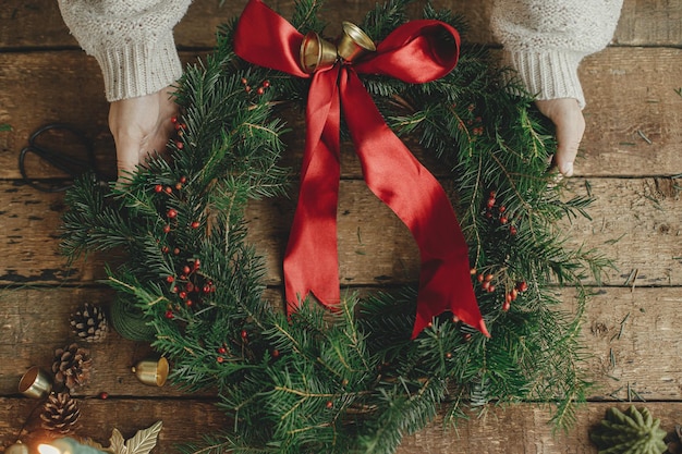 Couronne de Noël mise à plat Mains de femme tenant une couronne de Noël avec ruban rouge sur bois rustique