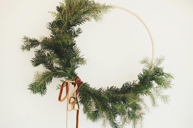 Couronne de Noël moderne avec ruban de velours et cloches dorées accrochées au mur blanc Joyeux Noël