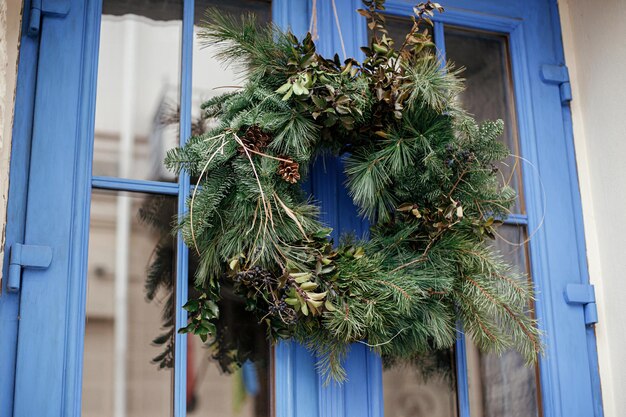 Couronne de Noël naturelle élégante sur les portes bleues de l'extérieur du bâtiment Décor de Noël écologique moderne dans la rue de la ville Vacances d'hiver en Europe Joyeux Noël et bonnes fêtes