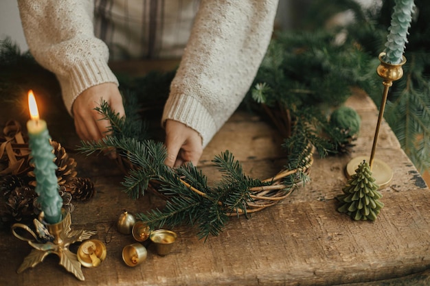 Couronne rustique de Noël Mains féminines tenant des branches de sapin et faisant une couronne sur une table en bois