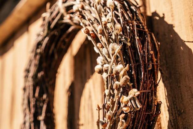 Couronne de saule suspendue étroitement tissée à partir d'osier avec des brindilles de coton décoratives et de la dentelle de ruban blanc Mur en bois et planches jaune rural sur fond Décoration de récolte saisonnière traditionnelle