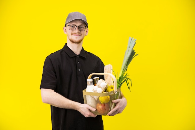 Courrier attrayant en uniforme noir tient le panier avec l'épicerie, la livraison de nourriture