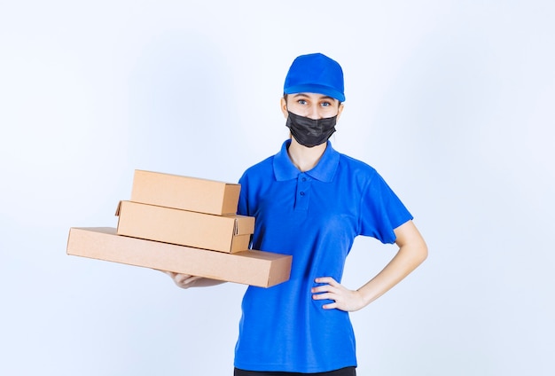 Courrier féminin en masque et uniforme bleu tenant un stock de boîtes en carton