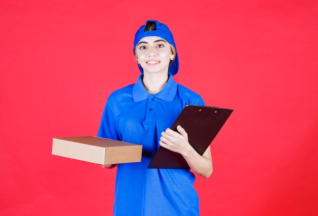 Courrier féminin en uniforme bleu tenant une liste de contrôle et donnant la boîte à emporter au client.