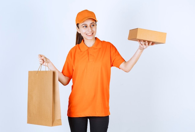 Courrier féminin en uniforme jaune livrant un sac à provisions et une boîte en carton au client