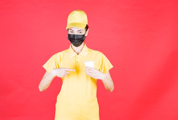 Courrier féminin en uniforme jaune et masque noir tenant une tasse à emporter