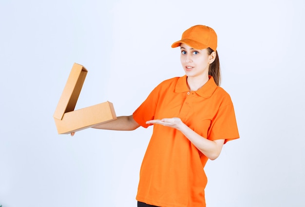 Courrier féminin en uniforme orange tenant une boîte en carton ouverte et a l'air confus et attentionné.