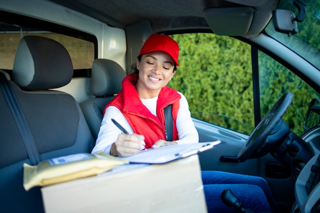 Courrier féminin en van vérifiant les documents avant de livrer l'envoi.