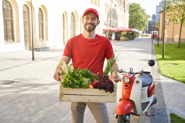 Courrier heureux en uniforme tenant une boîte d'épicerie avec des légumes frais