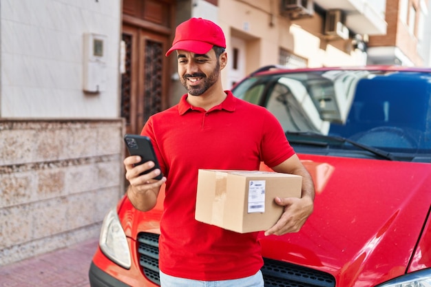 Courrier de jeune homme hispanique à l'aide d'un smartphone tenant un paquet dans la rue