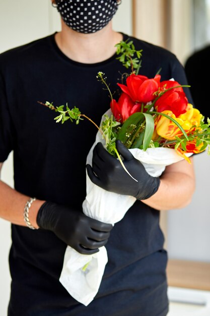 Courrier, livreur dans des gants en latex médical livre en toute sécurité des achats en ligne un bouquet de fleurs