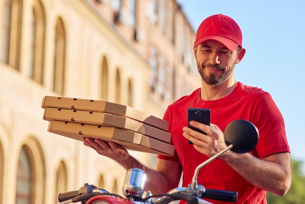 Courrier masculin caucasien souriant avec smartphone et pizza