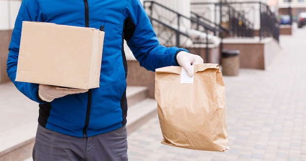 Courrier en masque de protection et gants médicaux livre des plats à emporter. Service de livraison en quarantaine, épidémie de maladie, conditions de pandémie de coronavirus covid-19.