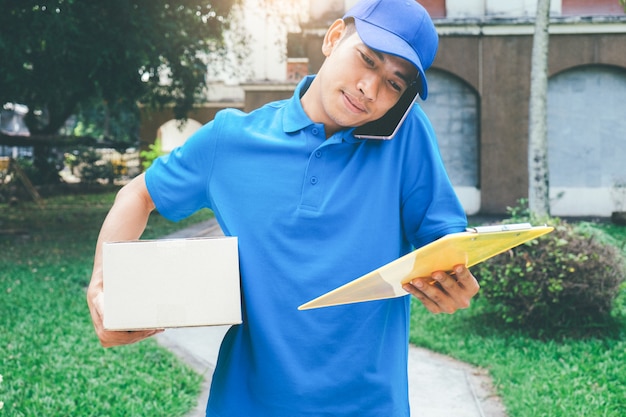 Courrier de service de livraison debout devant la maison avec des boîtes.