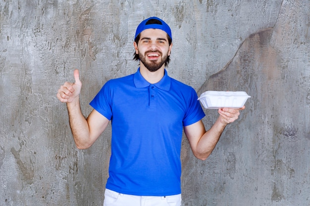 Photo courrier en uniforme bleu tenant une boîte à emporter en plastique et montrant un signe positif de la main.