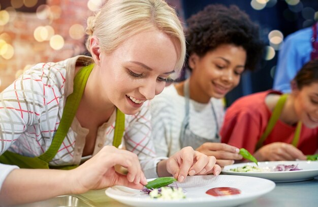 Photo cours de cuisine amitié nourriture et personnes concept femmes heureuses cuisiner et décorer des assiettes avec des plats dans la cuisine